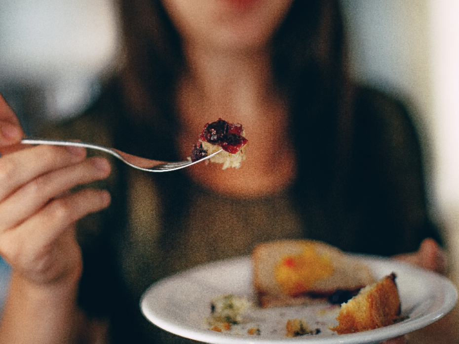 A person holding a fork and plate with food on it. 