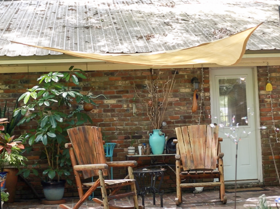 Two wooden chairs on a porch underneath a tan shade sail. 