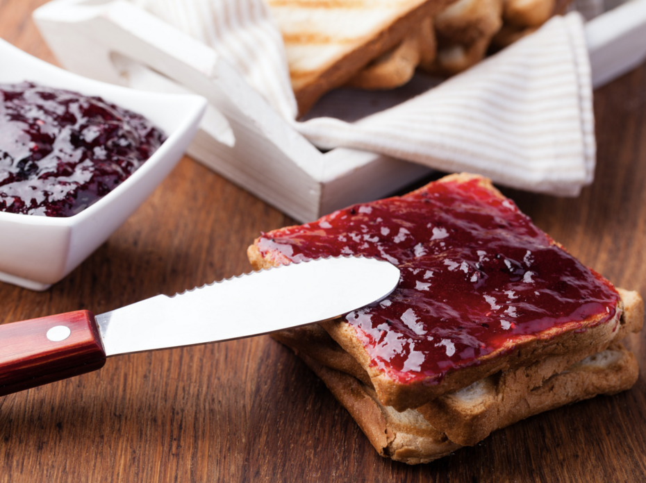 A knife spreading strawberry jam on toast.