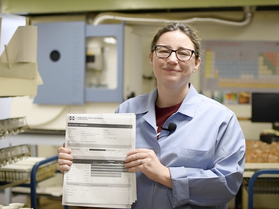 Woman in blue lab coat holding up paper.