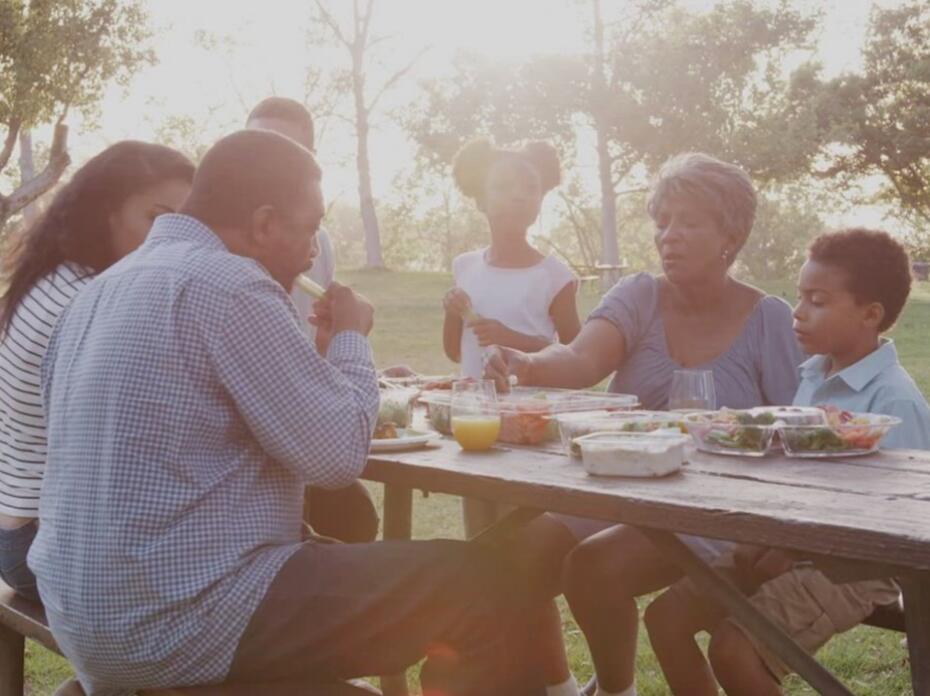 A family eats at a picnic table in the park.