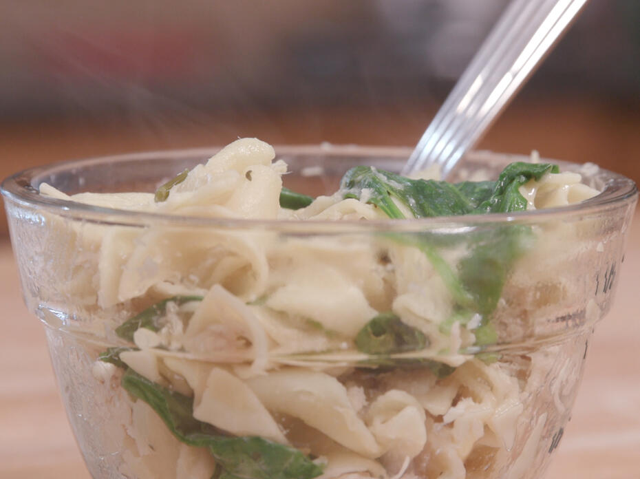 Cooked chicken, noodles, and spinach in a clear glass bowl