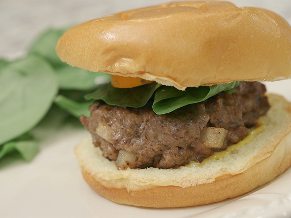 Venison burger on a bun sitting on a white plate.