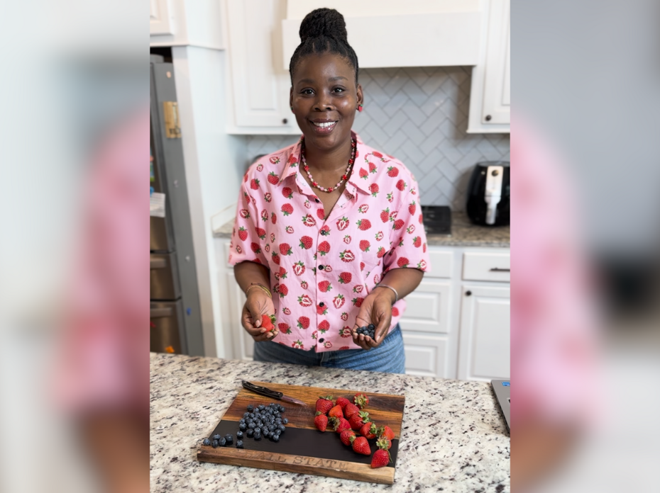 A woman stands in a kitchen with strawberries on a cutting board.
