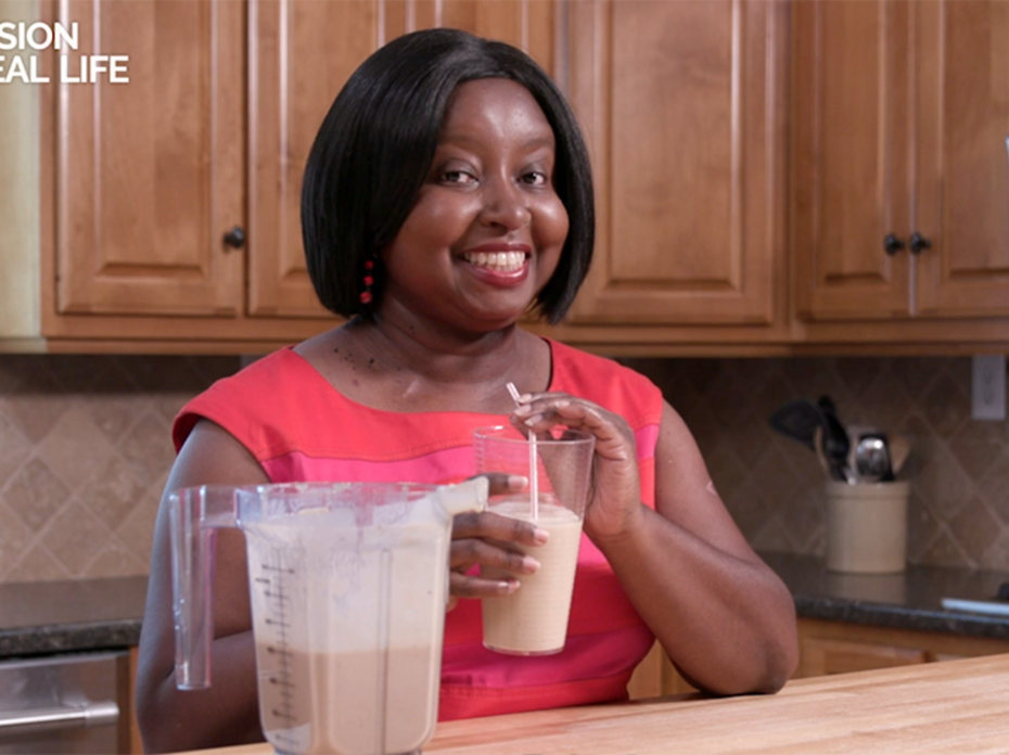 A woman holds a smoothie while standing in a kitchen.