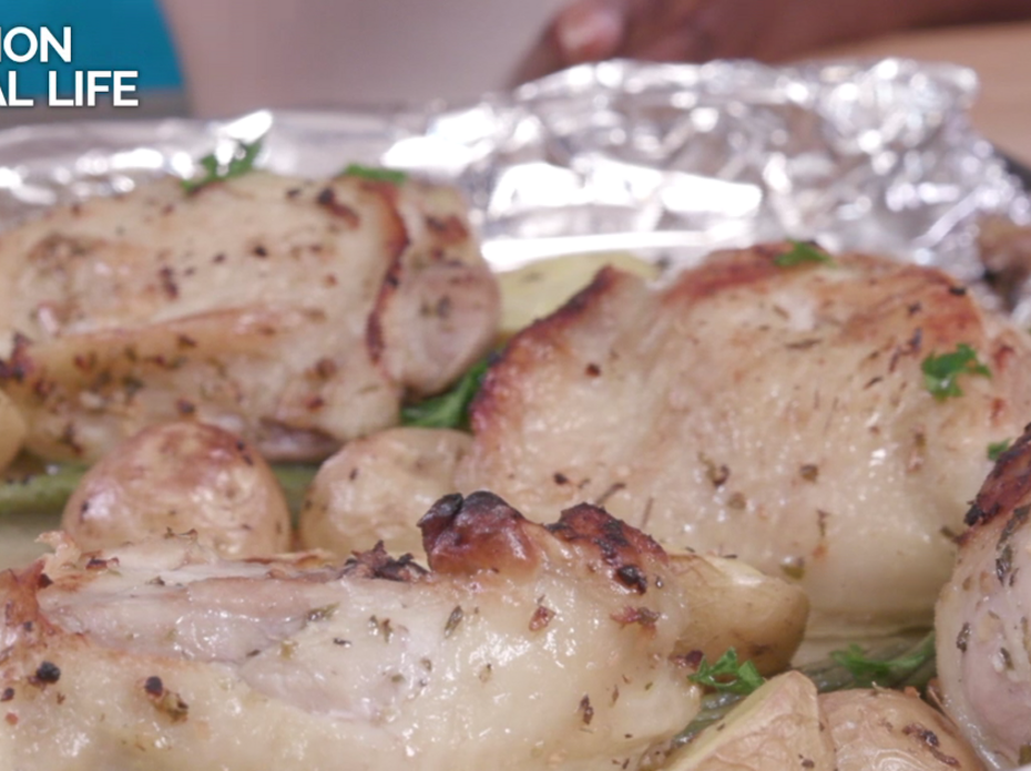 Several browned bone-in chicken thighs on top of halved baby potatoes and green beans on a foil-covered sheet pan.