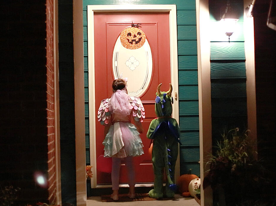 Two children waiting at a well-lit door for Halloween treats.