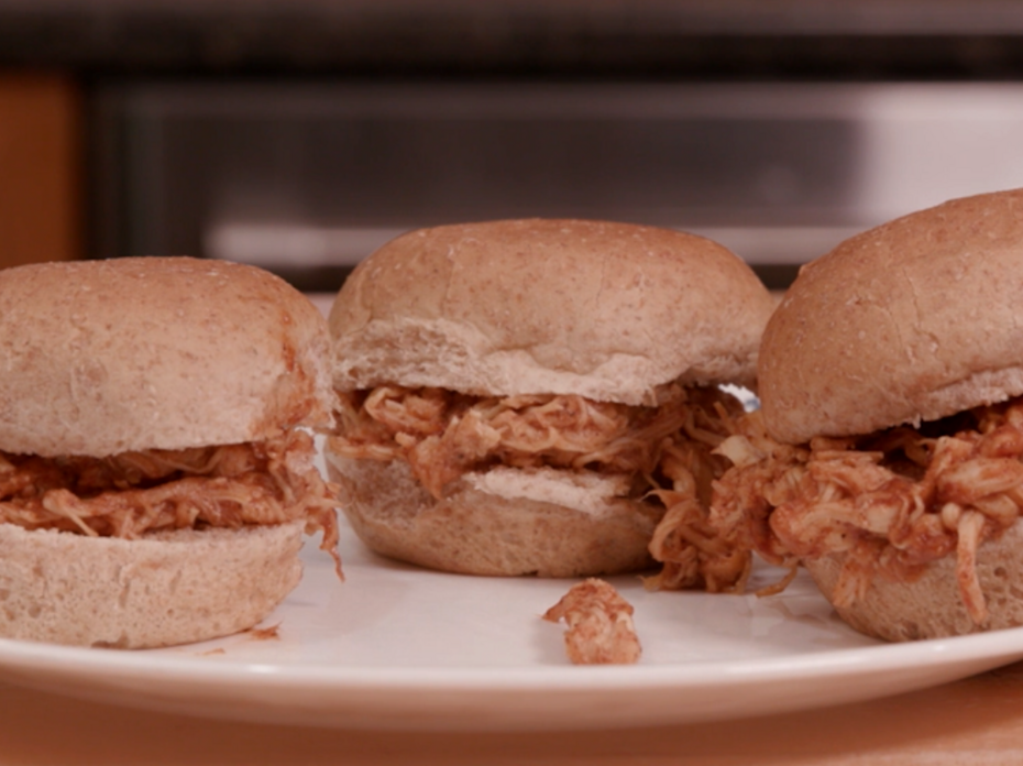 Three small sandwiches made with whole wheat slider buns, shredded chicken, and barbecue sauce on a white plate. 