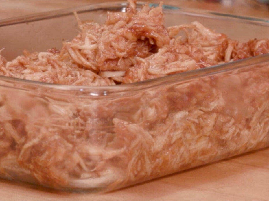 Shredded chicken breasts coated in barbecue sauce in a rectangular, clear-glass container.