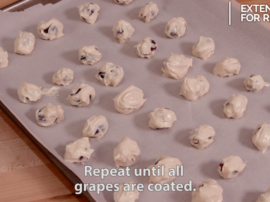 Red grapes dipped in a mixture of peanut butter and Greek yogurt lined up on a parchment paper covered baking sheet. 