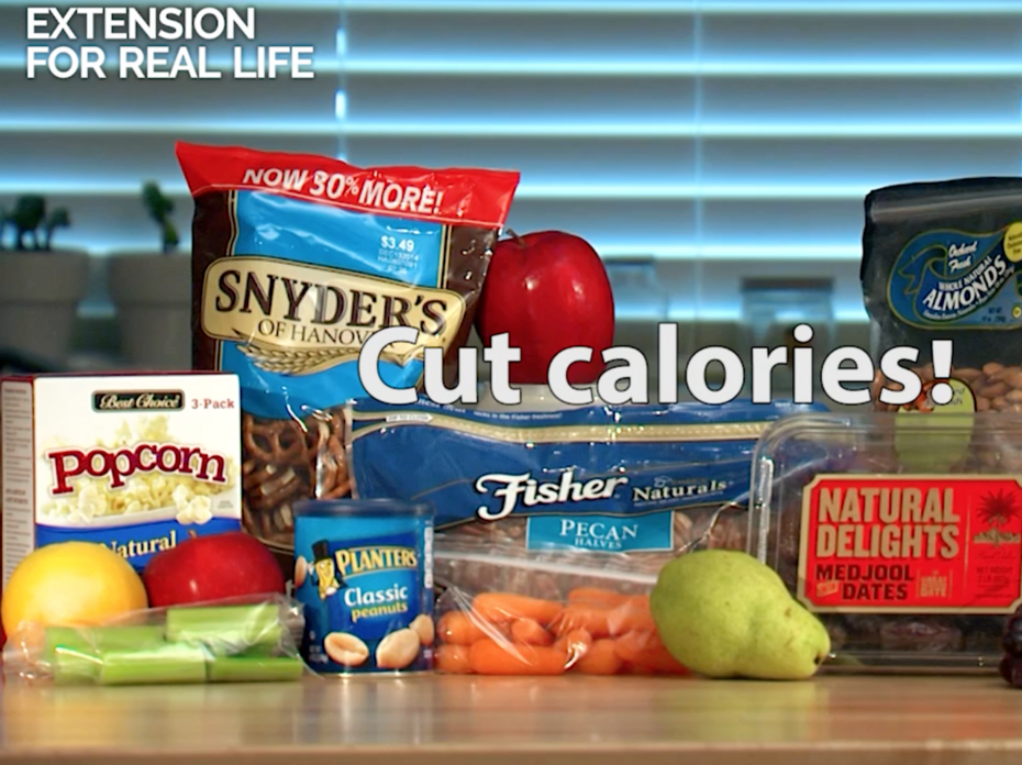 An assortment of snack foods on a butcher block table top, including a green pear, red grapes, baby carrots, pretzels, pecans, dates, almonds, and trail mix. 