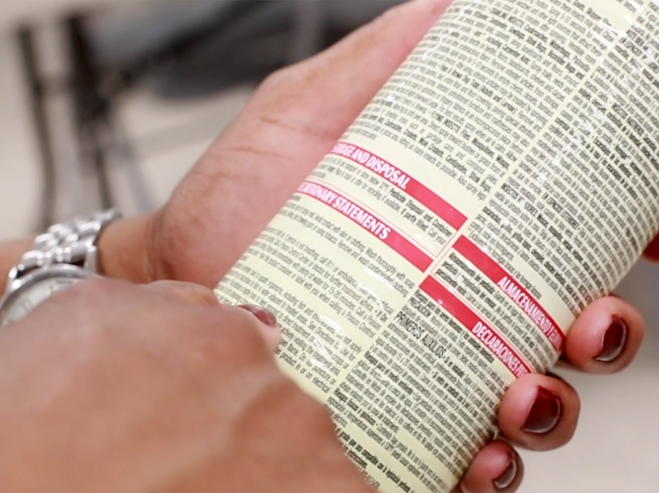 A closeup of a woman's hands holding a pesticide container while reading the instructions.