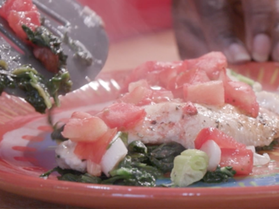 Baked fish with spinach, tomatoes, and onions sits on a plate.