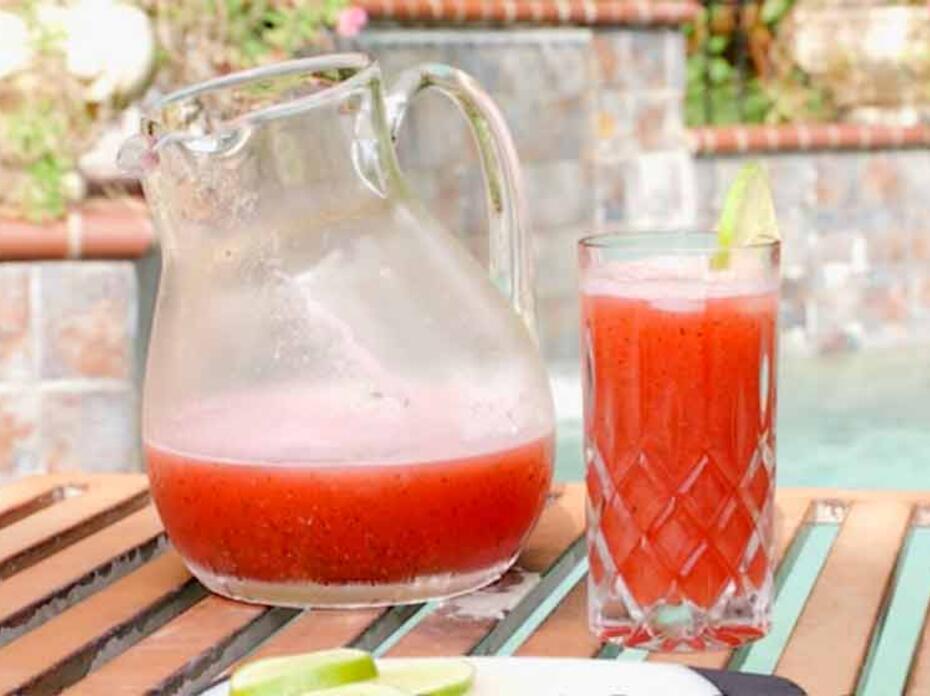 A clear glass pitcher and glass with watermelon punch. 