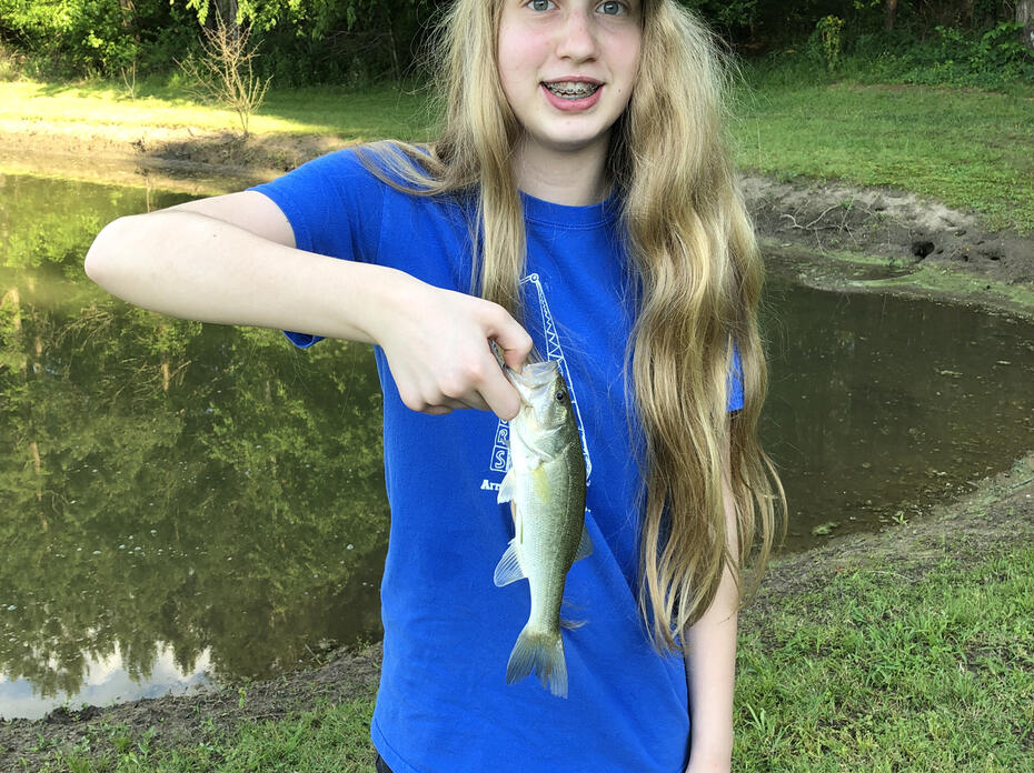 Girl in a blue T-shirt and baseball cap holding a small fish.