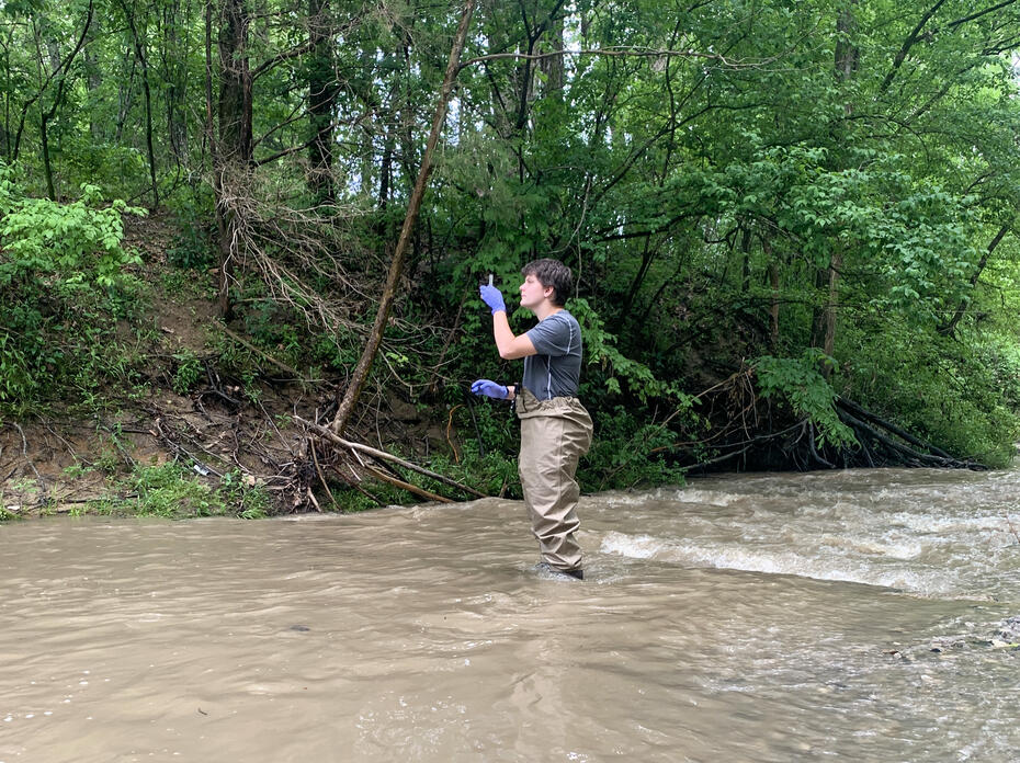 Woman in wading pants collects a water sample in a creek.