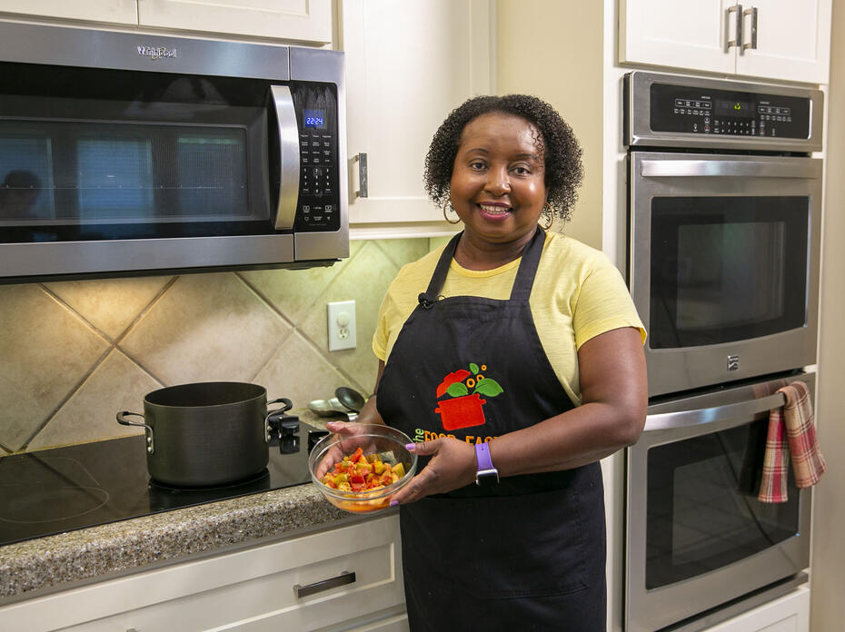 A woman stands in front of the stove with a bowl of Catfish Gumbo.