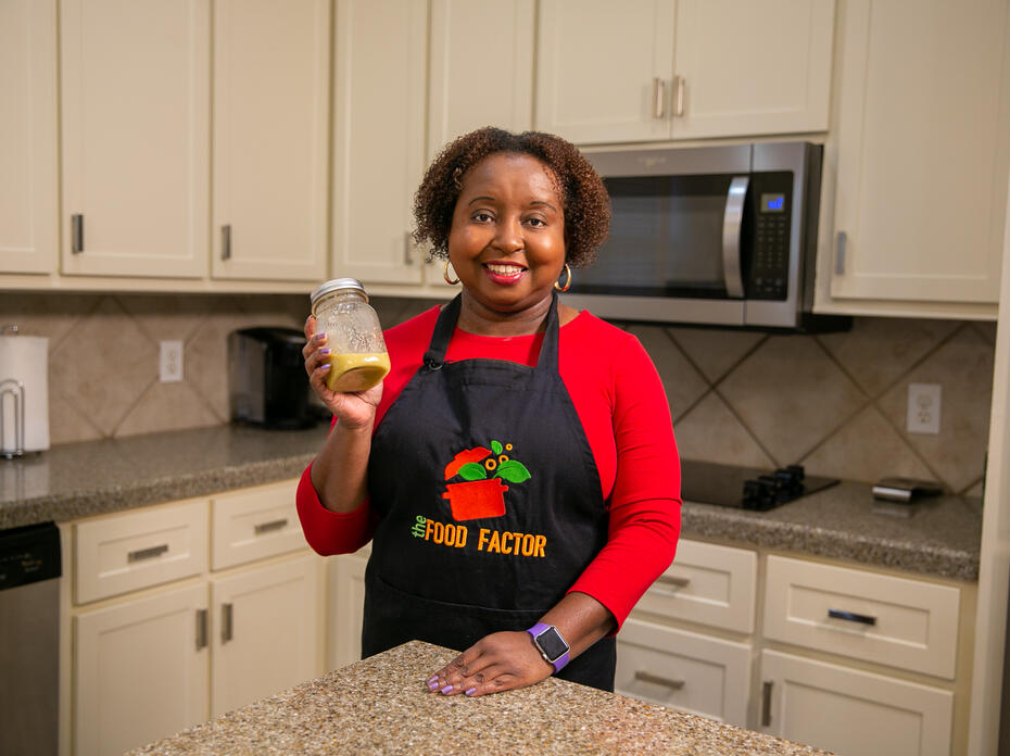 A woman holds a jar of Honey Mustard Dressing in a kitchen.