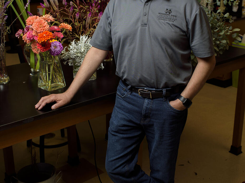 A man stands at a table holding floral arrangements.