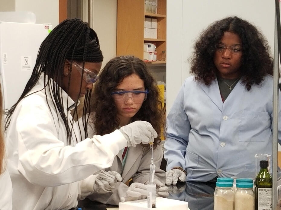 Three girls in lab coats work with scientific equipment.