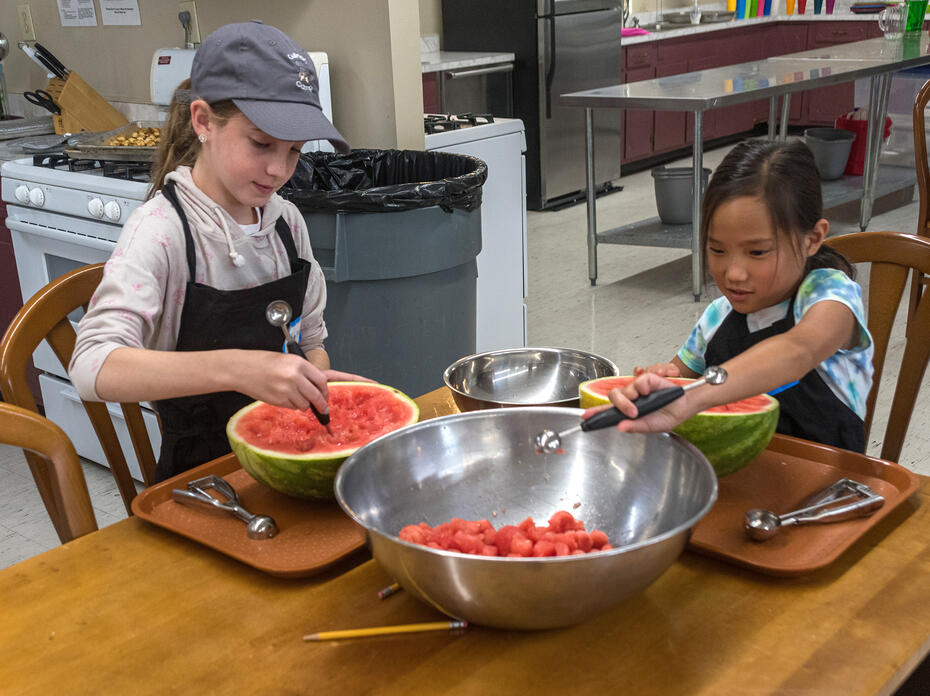 Two children make melon balls from a watermelon.