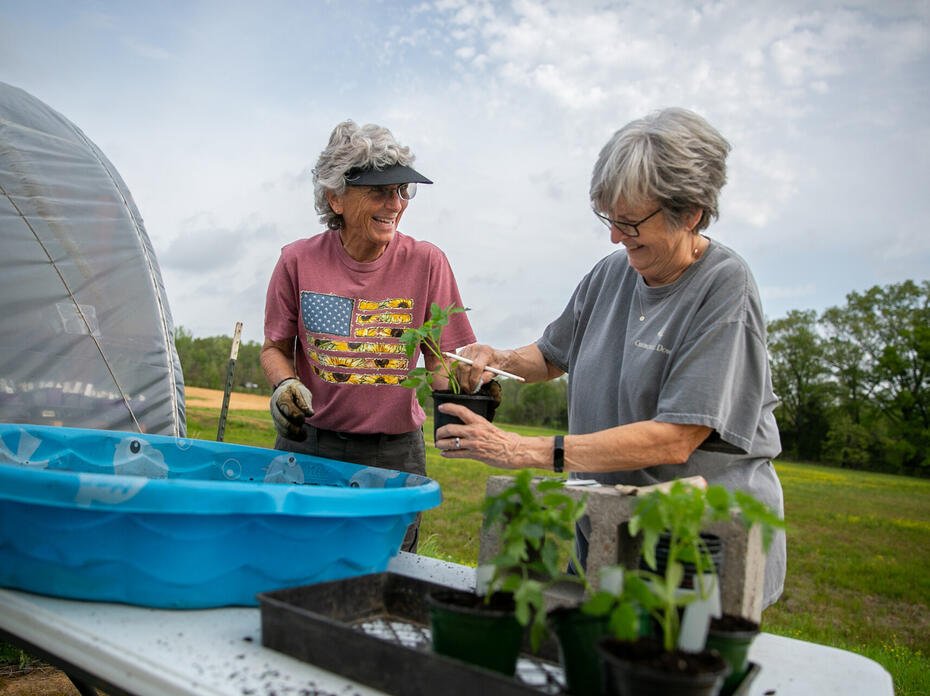 Two women work with potted plants outdoors.