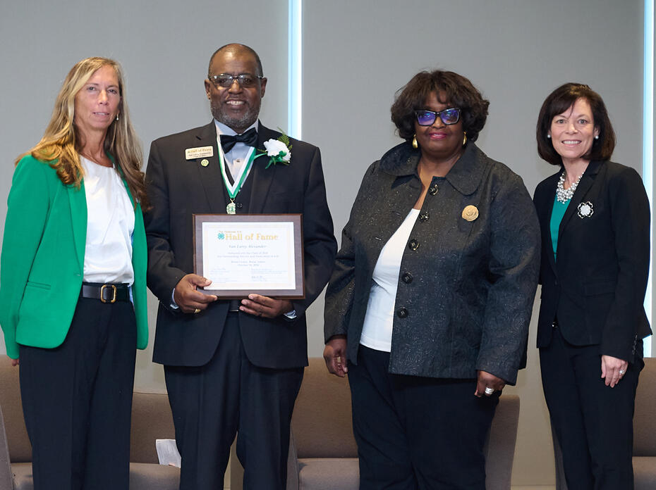 Four people stand in a line for a plaque presentation.