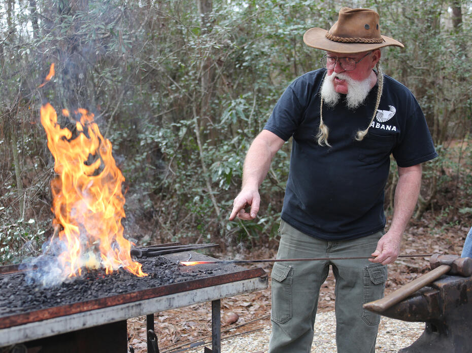 A man points at hot metal he just heated in a fire to forge it.