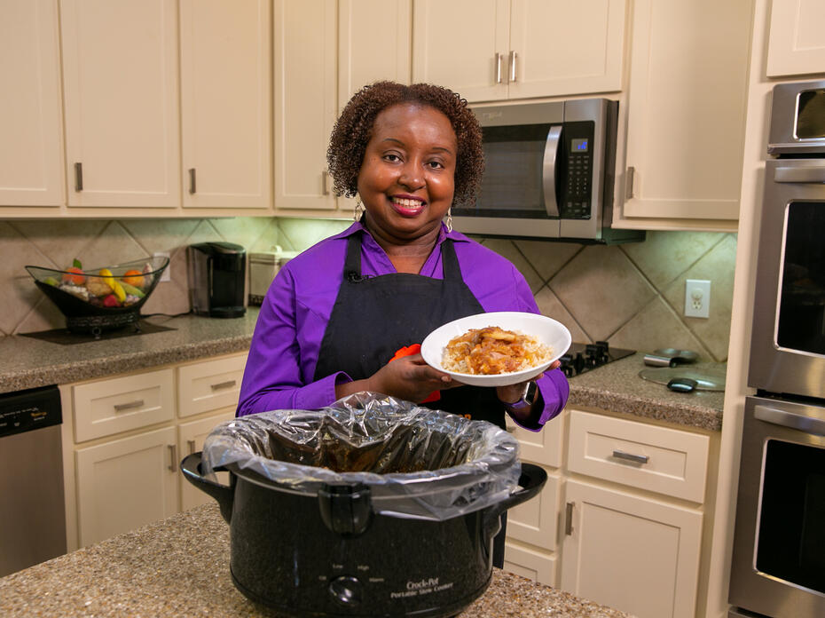 A woman stands in a kitchen and holds a serving of Chicken with Peachy Ginger Sauce.