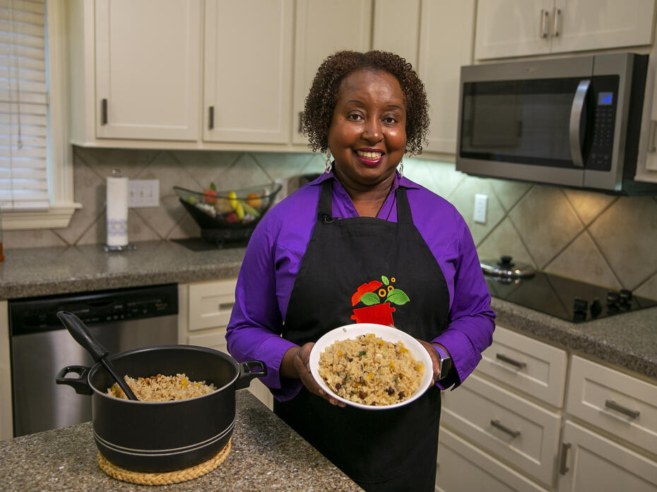 A woman stands in a kitchen with a bowl of rice pilaf posing for the camera.