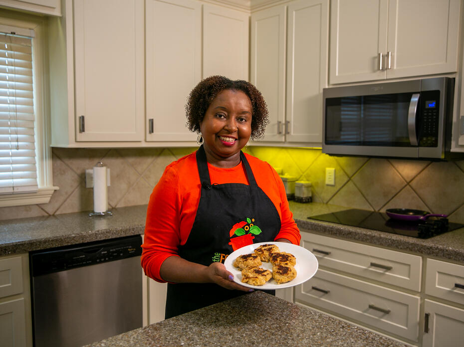 A woman stands in a kitchen holding a plate of salmon patties for the camera.