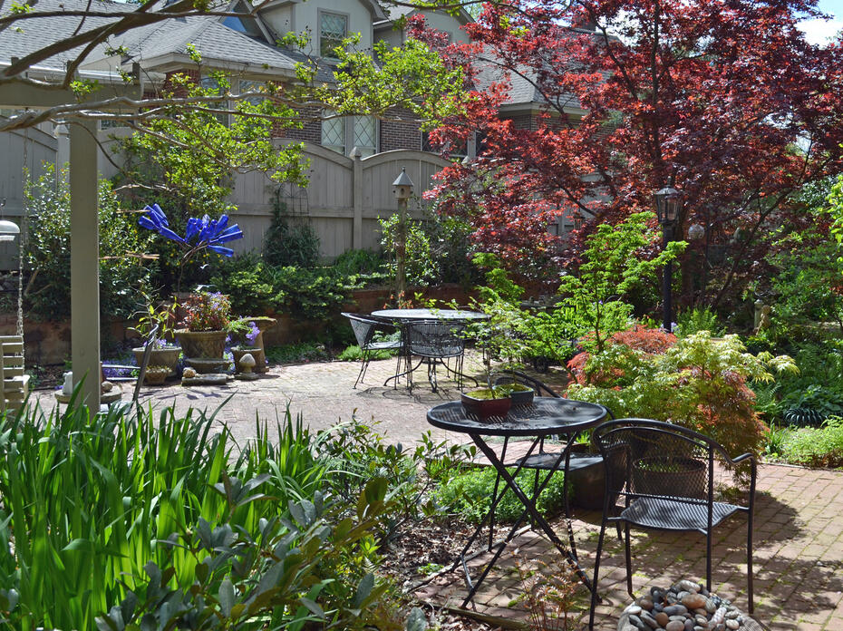 Tables and chairs are on a patio in a backyard garden.