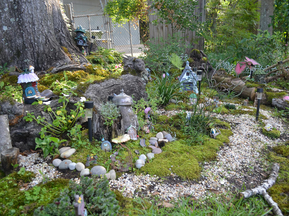 A pea gravel trail surrounds a miniature fairy village under a tree.
