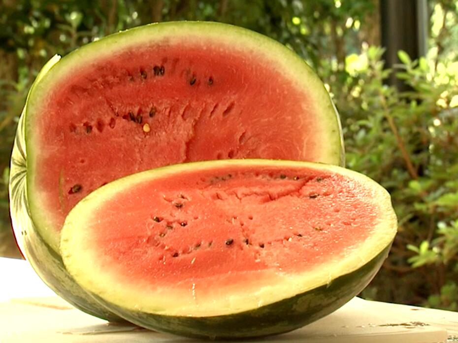 A sliced, ripe watermelon sits on a table outdoors.
