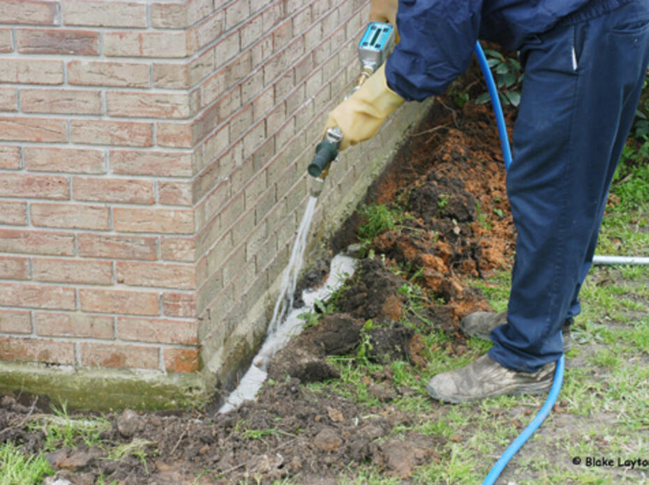 A pesticide technichian applies a termite treatment around a home foundation.