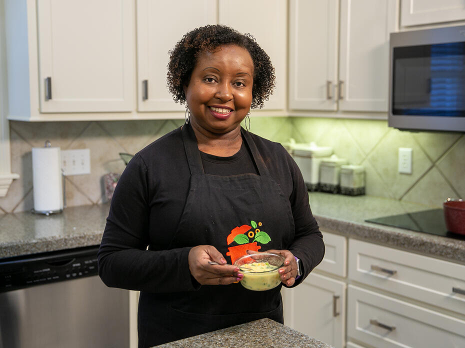 A woman stands in a kitchen and holds a bowl of soup.