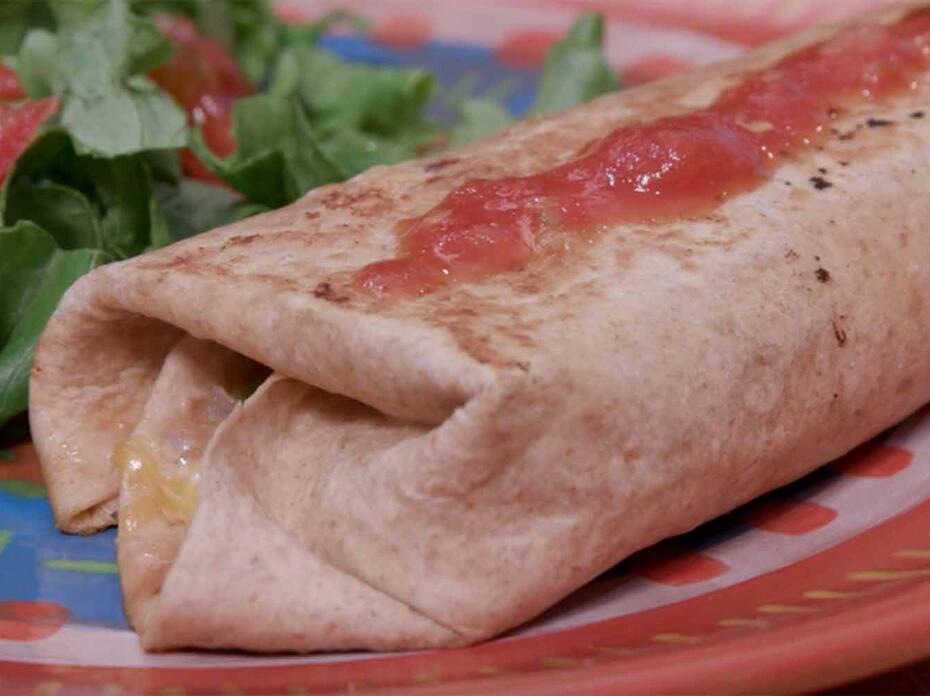 A grilled burrito topped with salsa and a green salad with tomato served on a multicolored plate.
