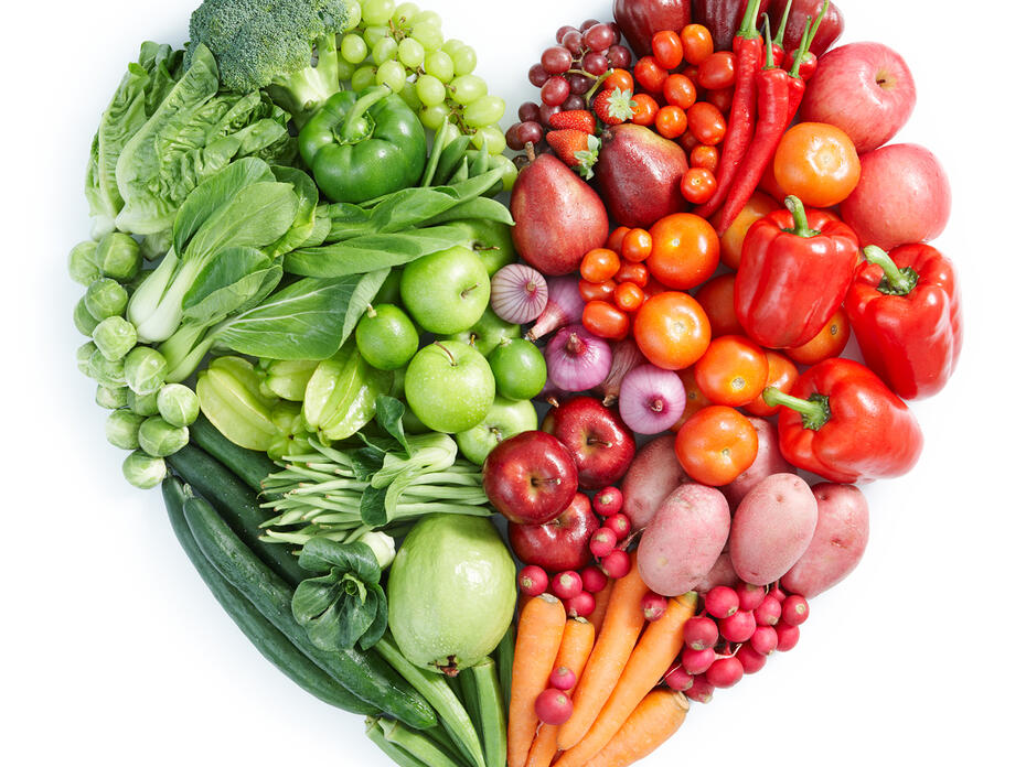 An assortment of green, orange, and red vegetables are arranged in a heart shape. 