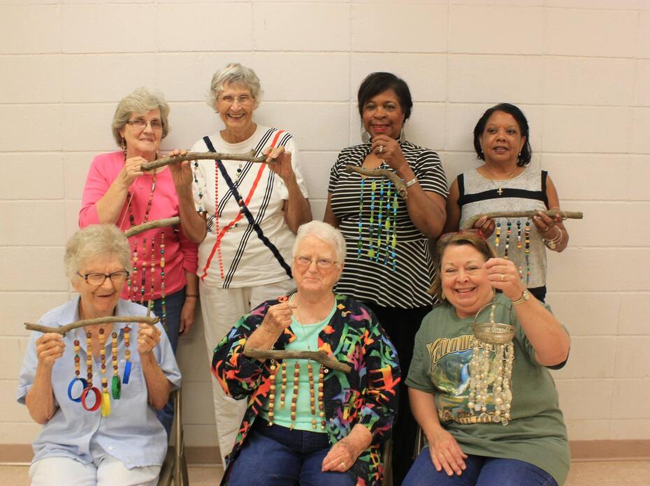 Seven women smile as they hold beaded windchimes.