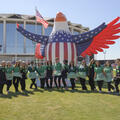 Fifteen young people wearing green jackets stand in front of an inflatable eagle.
