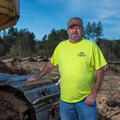 A smiling person standing next to a bulldozer at a logging site.