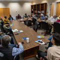A large group of people seated around a table in a conference room.