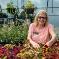 A person smiling in a greenhouse surrounded by colorful foliage.