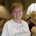 A woman stands smiling in front of a room full of people working at long tables.