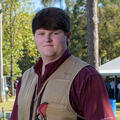 A teenage boy stands outside with a firearm resting on his shoulder.