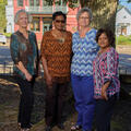 Four women stand next to each other under the shade of a tree.