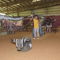 A young boy throws a rope toward a fake bull with the help of an older man standing behind him.