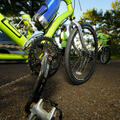 A close up shot of the gears and bottom of a fluorescent green bike parked in a parking lot.