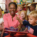 A woman happily reading a book to several small children.