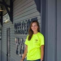 A teen with brown hair and wearing a green Junior Master Wellness Volunteer T-shirt stands in front of the Cleveland, Mississippi, Welcome Center.